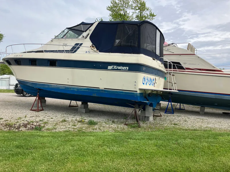 Slide: The Image of 1985 Cruisers 336 Ultra Vee boat on stands, parked on gravel near grass. - 3