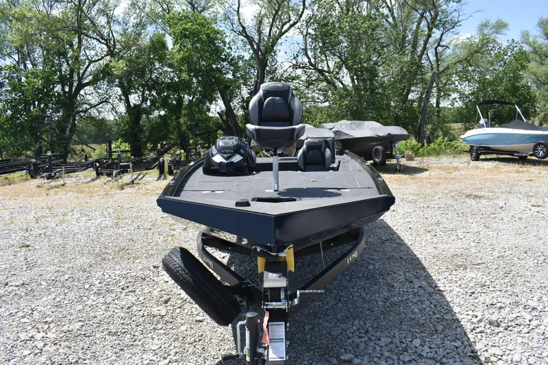 Slide: The Image of 2025 Lund 1875 Renegade SS boat on gravel, surrounded by trees and other boats. - 2