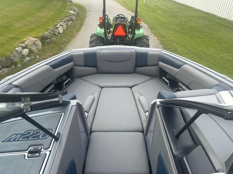 Slide: The Image of 2022 Malibu M220 boat interior with gray seating, parked near a green tractor. - 13