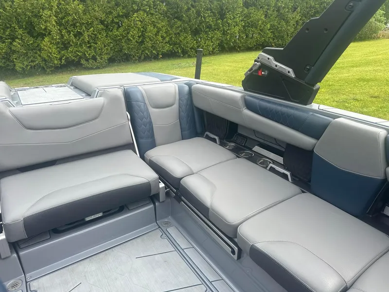 Slide: The Image of 2022 Malibu M220 boat interior with gray and blue seating, surrounded by greenery. - 25