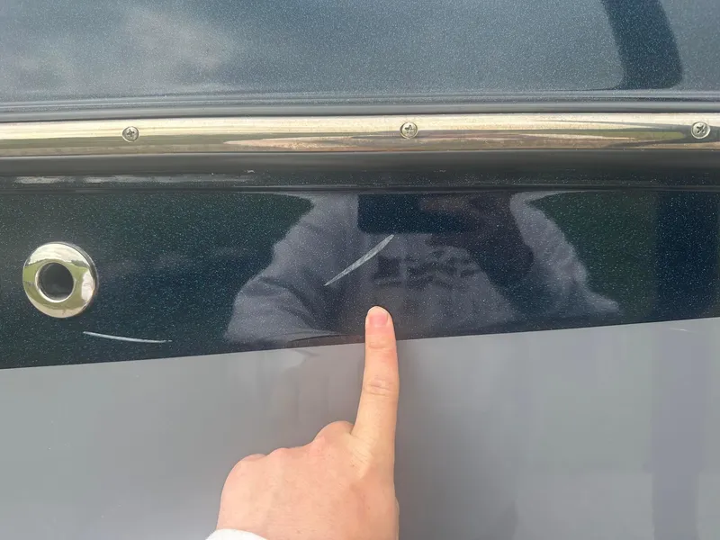 Slide: The Image of 2022 Malibu M220 boat with visible scratch on the side, finger pointing at damage. - 29