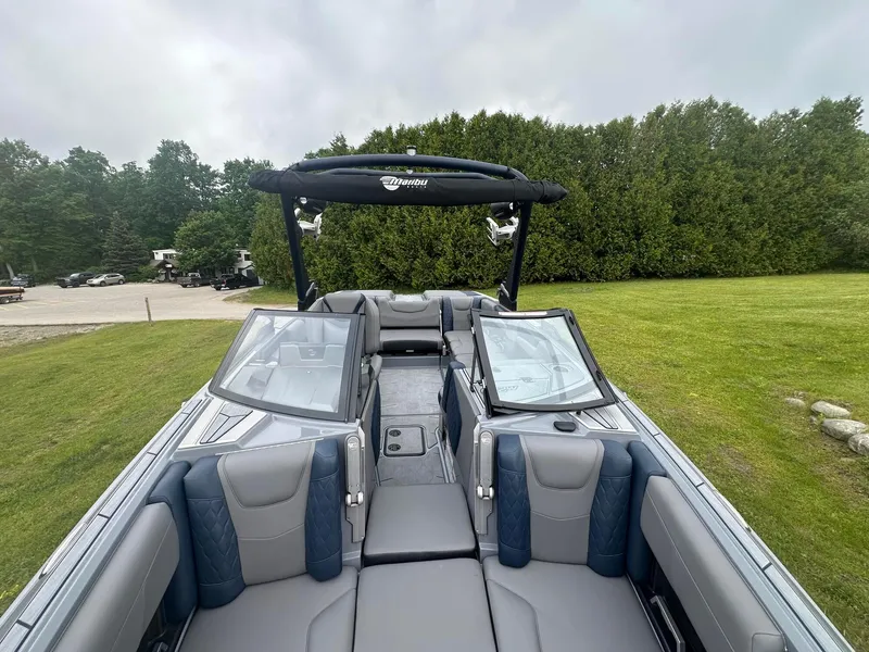 Slide: The Image of 2022 Malibu M220 boat interior with sleek seating and windshield, parked on grassy area. - 3