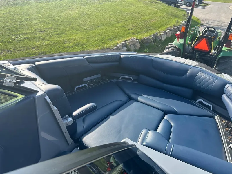 Slide: The Image of 2020 Malibu M240 boat interior with blue seating, parked near green grass and a tractor. - 13