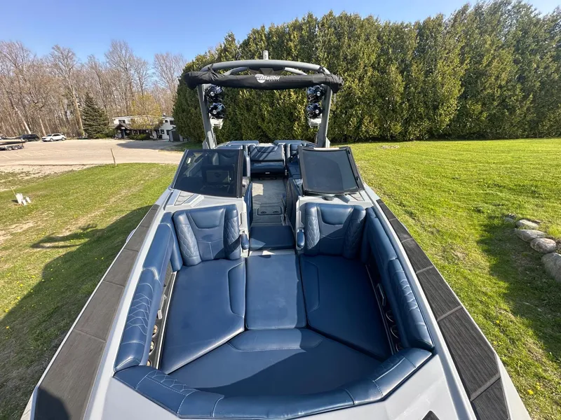 Slide: The Image of 2020 Malibu M240 boat with blue interior, parked on grass, surrounded by trees. - 30
