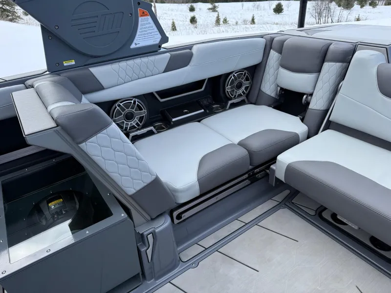 Slide: The Image of 2021 Malibu M240 boat interior with gray and white seating, featuring speakers and quilted upholstery. - 12