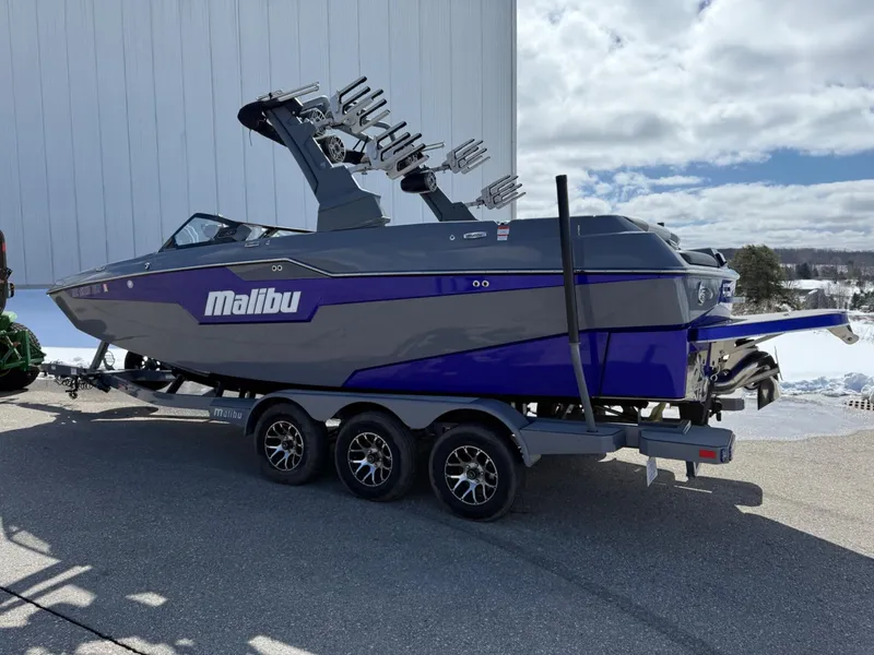 Slide: The Image of 2021 Malibu M240 boat on trailer, gray and blue design, parked outdoors. - 5