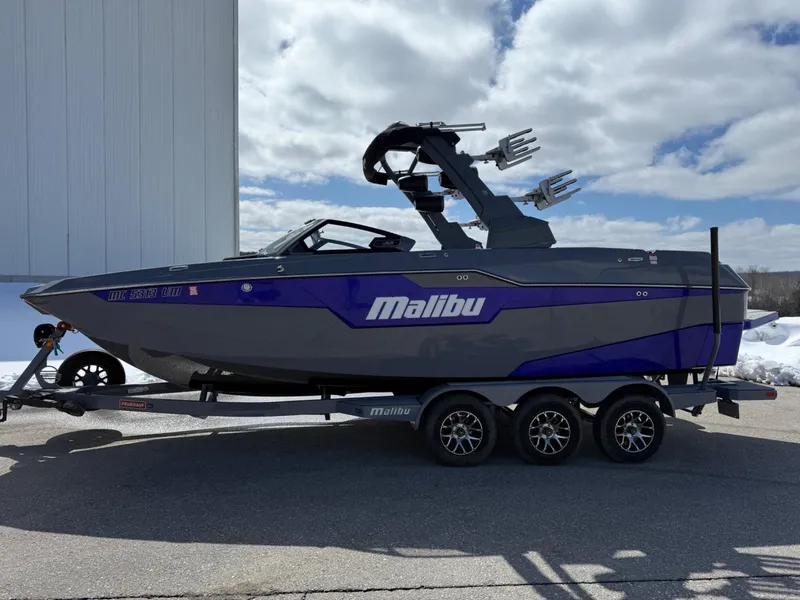 Slide: The Image of 2021 Malibu M240 boat on trailer, gray and blue design, parked outdoors under cloudy sky. - 6