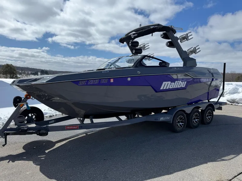 Slide: The Image of 2021 Malibu M240 boat on trailer, gray and purple, parked outdoors under cloudy sky. - 7