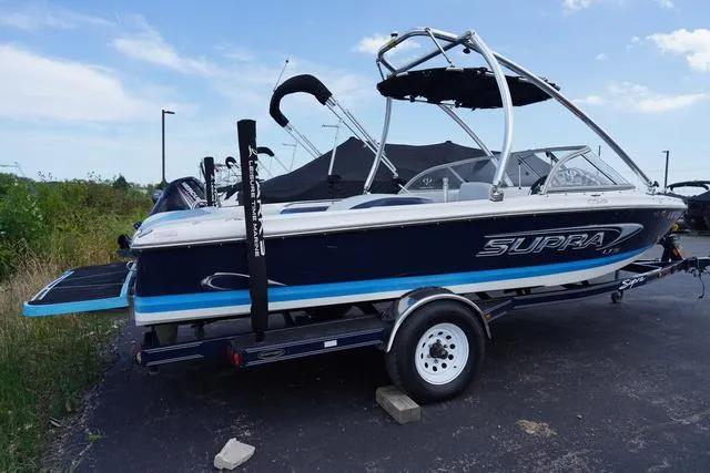 Slide: The Image of 2004 Supra COMP LTS/SK boat on trailer, blue and white design, parked outdoors. - 3