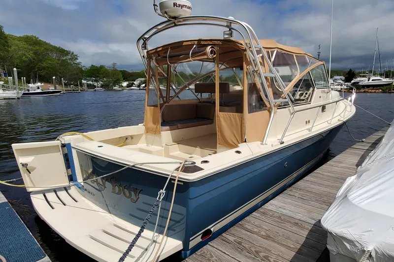 Slide: The Image of 2006 Mainship 34 Rum Runner Classic docked, featuring a blue hull and tan canopy. - 1