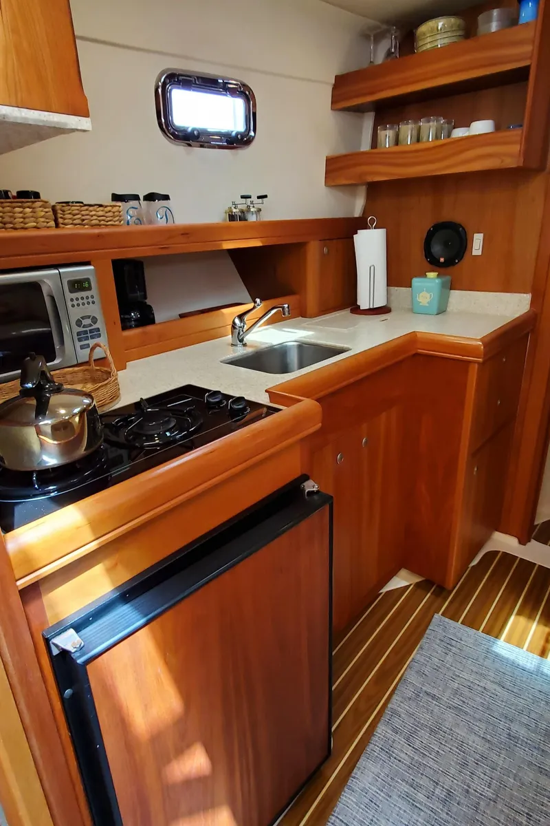 Slide: The Image of 2006 Mainship 34 Rum Runner classic galley with wood cabinetry, stove, sink, and compact fridge. - 18