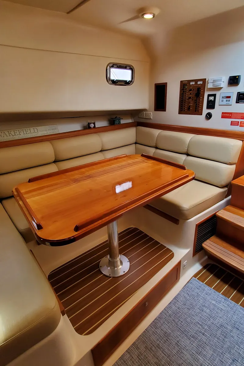 Slide: The Image of 2006 Mainship 34 Rum Runner Classic interior with wooden table and cushioned seating. - 22