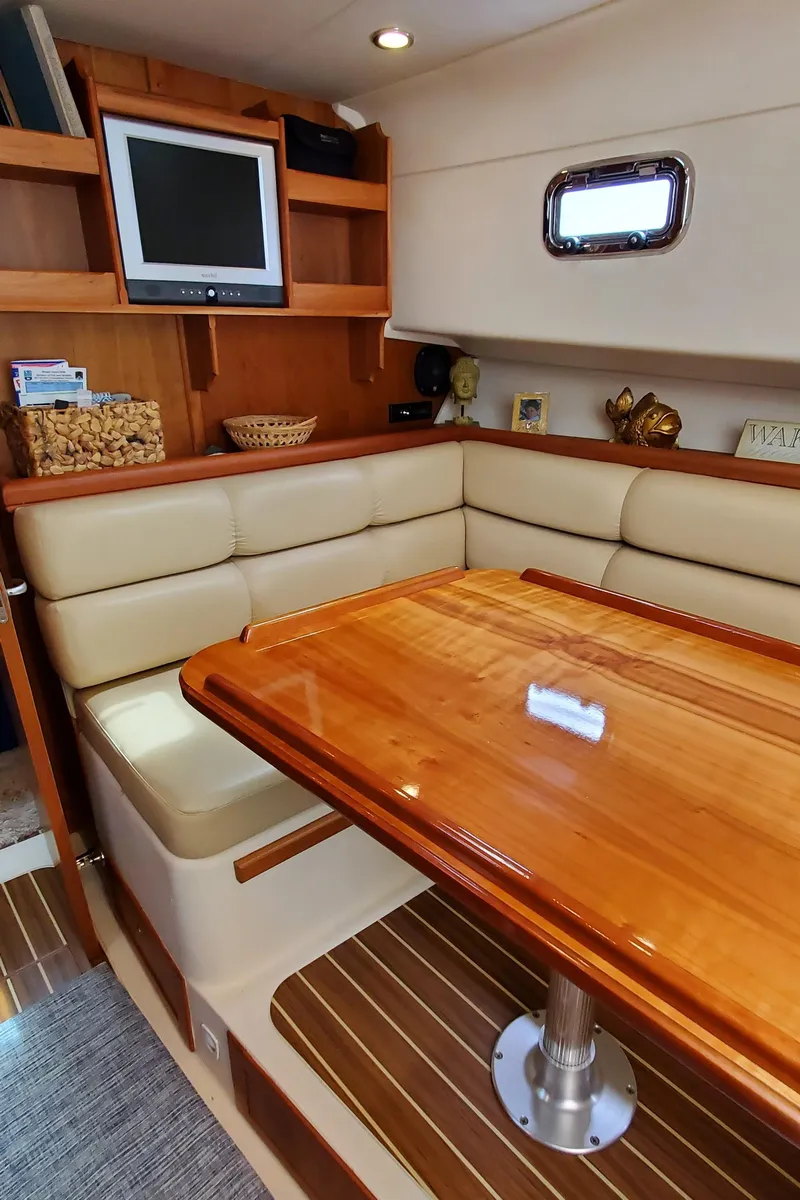 Slide: The Image of 2006 Mainship 34 Rum Runner classic interior with wood table, cushioned seating, and TV. - 23