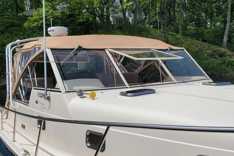 Slide: The Image of 2006 Mainship 34 Rum Runner Classic boat with tan canopy, docked near lush greenery. - 5