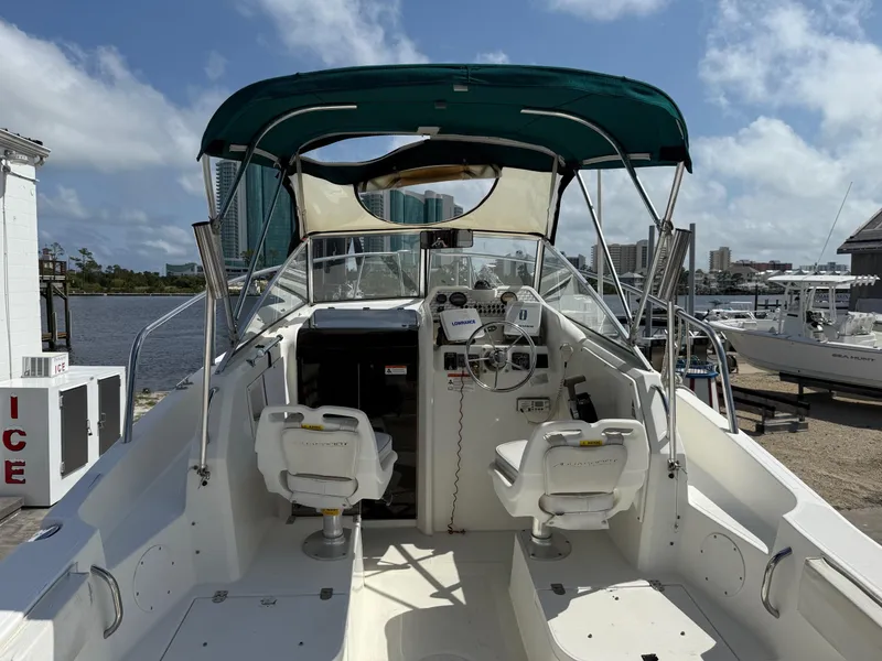 Slide: The Image of 2004 Aquasport 250 Explorer boat with canopy, docked by the waterfront under a clear sky. - 22