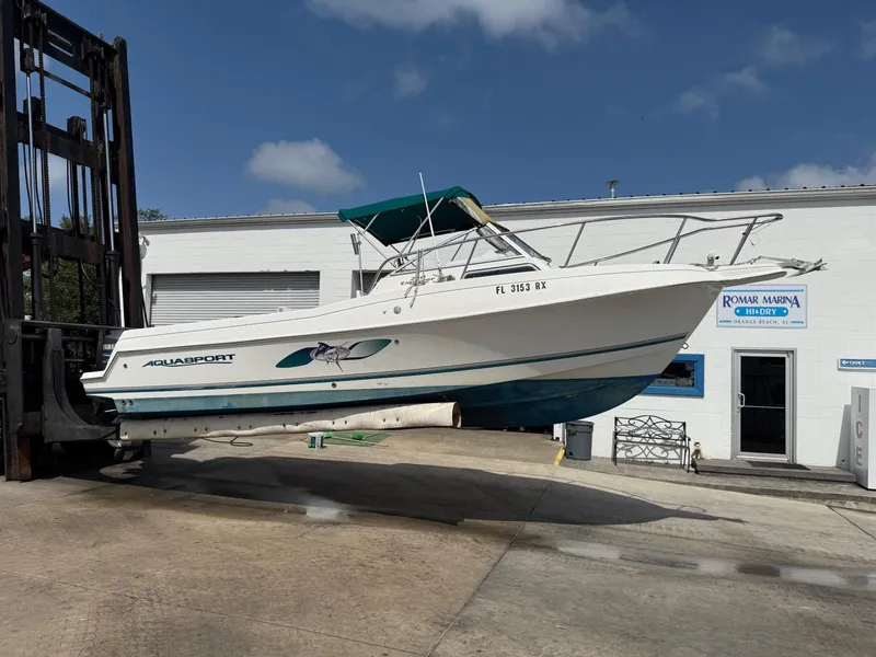 Slide: The Image of 2004 Aquasport 250 Explorer boat lifted at marina, clear sky background. - 5