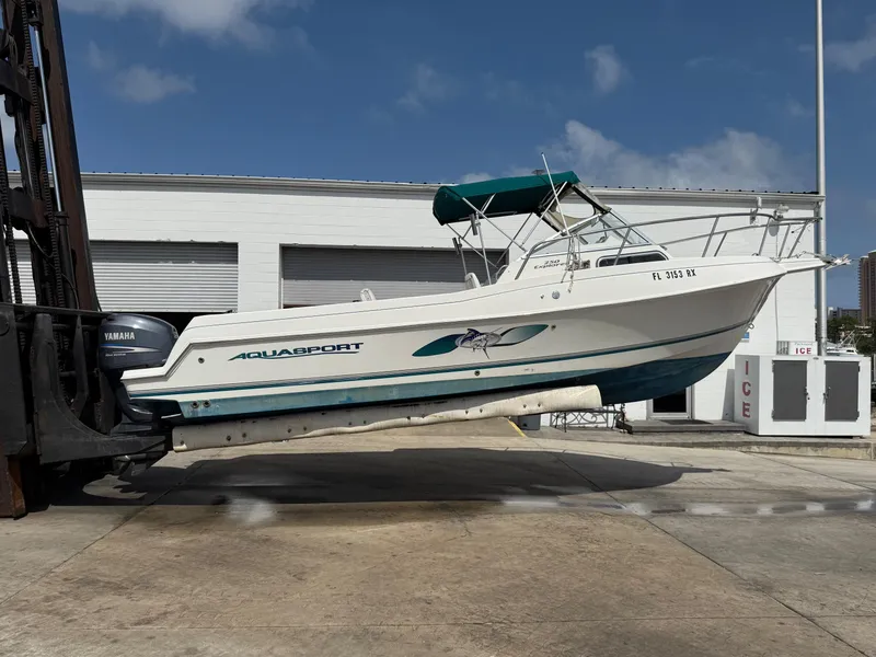 Slide: The Image of 2004 Aquasport 250 Explorer boat on forklift, white hull, green canopy, outdoor setting. - 6