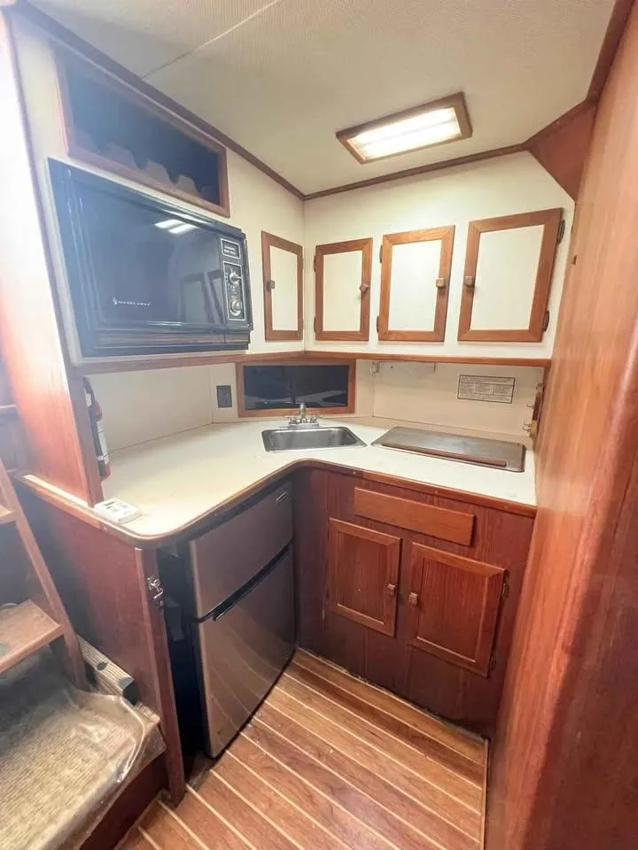 Slide: The Image of 1988 Topaz 37 Sportfisherman kitchen with wood cabinets, compact fridge, and microwave. - 3