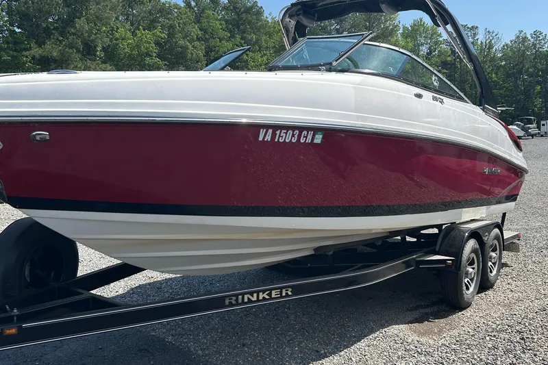 Slide: The Image of 2018 Rinker 26QX BR boat on trailer, red and white, parked on gravel. - 3
