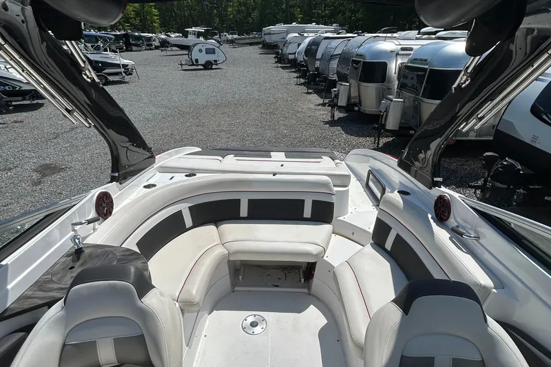 Slide: The Image of 2018 Rinker 26QX BR boat interior with seating, parked near RVs and trailers. - 8