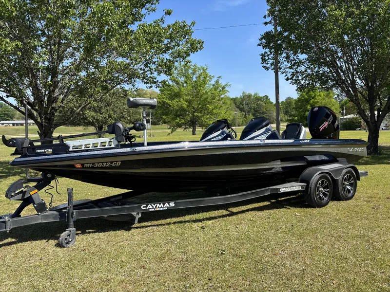 Slide: The Image of 2022 Caymas CX21 Pro boat on trailer, parked on grass with trees in background. - 2
