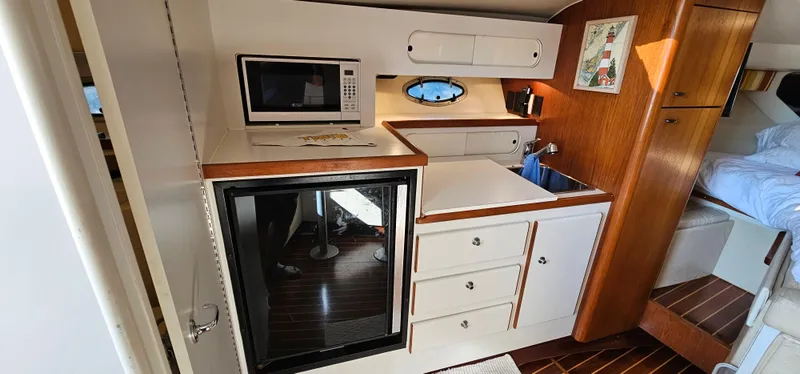 Slide: The Image of 1994 Tiara Yachts 3100 Open galley with microwave, fridge, sink, and wooden cabinetry. - 30