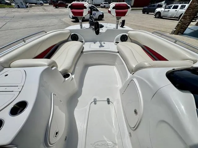 Slide: The Image of 2014 Tahoe 215 Xi boat interior with white seating and red accents, parked outdoors. - 12