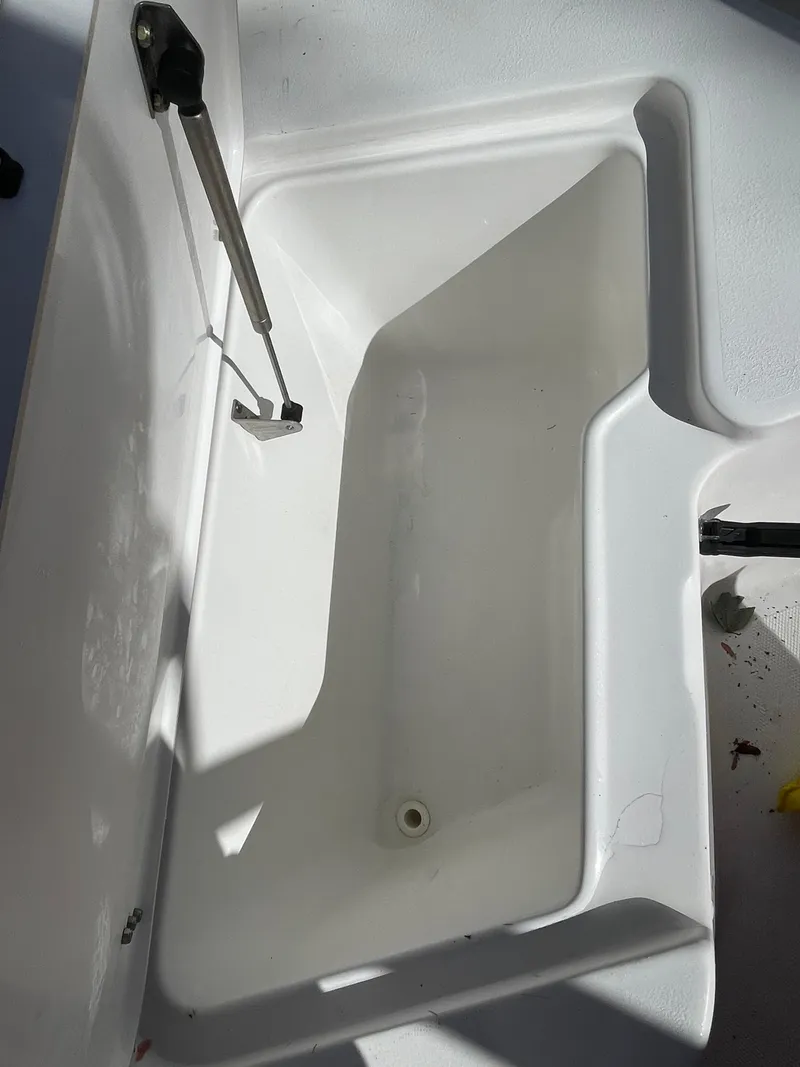 Slide: The Image of 2017 Sea Hunt 225 Ultra boat storage compartment, open lid, white interior, shadowed lighting. - 25