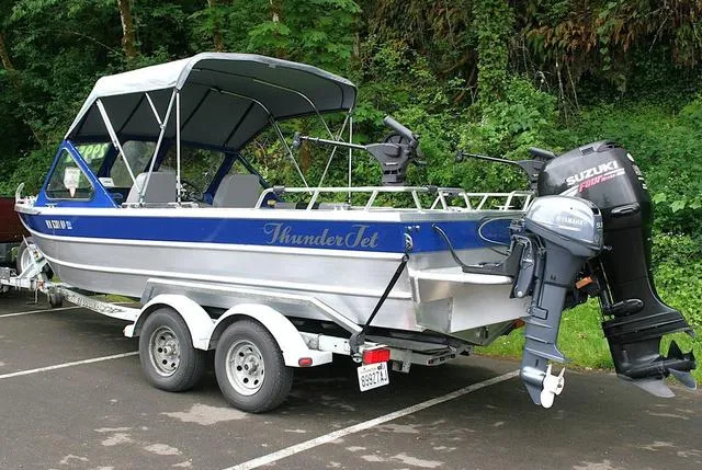 Slide: The Image of 2003 Thunder Jet 19 Luxor boat with Suzuki outboard motor on trailer, parked near lush greenery. - 3