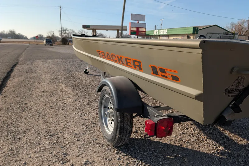 Slide: The Image of 2025 Tracker Grizzly 15 Jon boat on trailer, parked roadside near a store. - 21