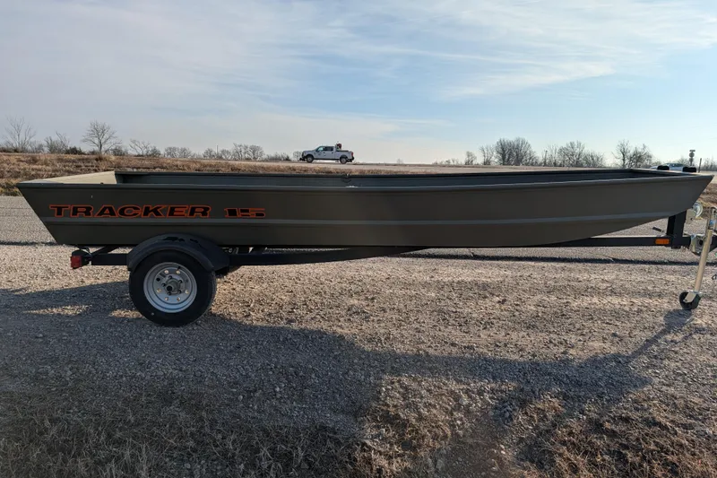 Slide: The Image of 2025 Tracker Grizzly 15 Jon boat on trailer, parked on gravel road under clear sky. - 25