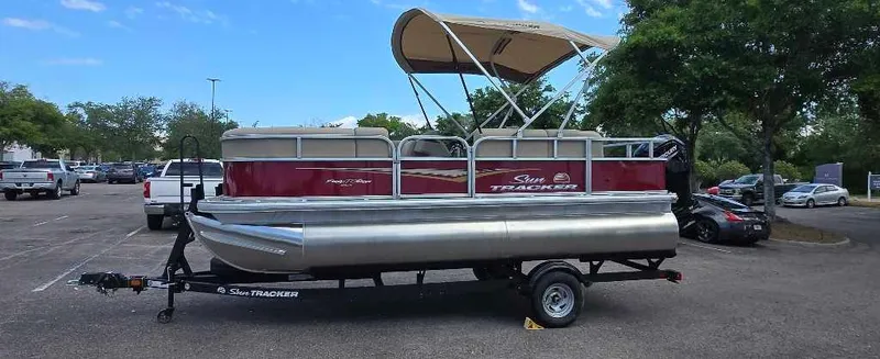 Slide: The Image of 2025 Sun Tracker Bass Buggy 16 XL Select pontoon boat on trailer in parking lot. - 2