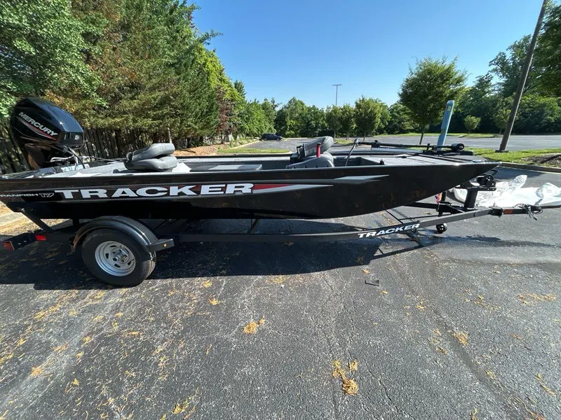 Slide: The Image of 2025 Tracker Panfish 17 boat on trailer, parked outdoors, surrounded by trees. - 2