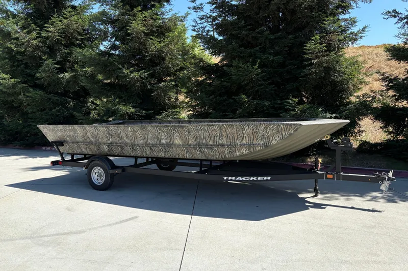 Slide: The Image of 2025 Tracker Grizzly 2072 Utility boat on trailer, parked outdoors near trees. - 2