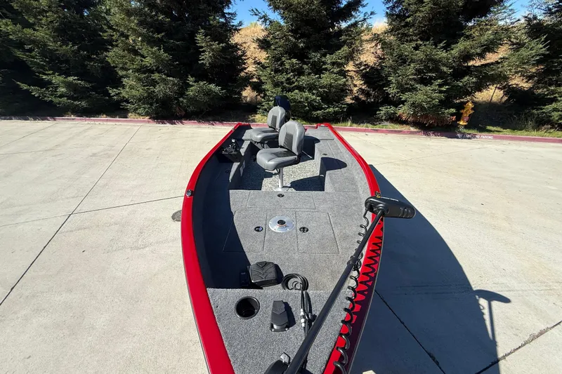Slide: The Image of 2025 Tracker Super Guide V-16 T boat with red trim, parked on concrete near trees. - 4