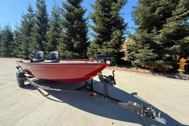 Slide: The Image of 2025 Tracker Super Guide V-16 T boat on trailer, parked outdoors near trees. - 2