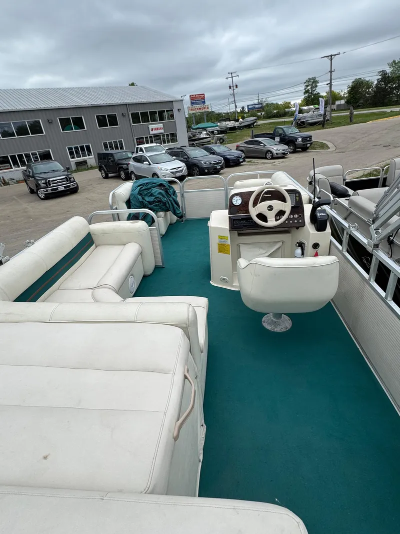 Slide: The Image of 1996 Premier Odyessea boat interior with white seating and teal flooring, parked near a dealership. - 15