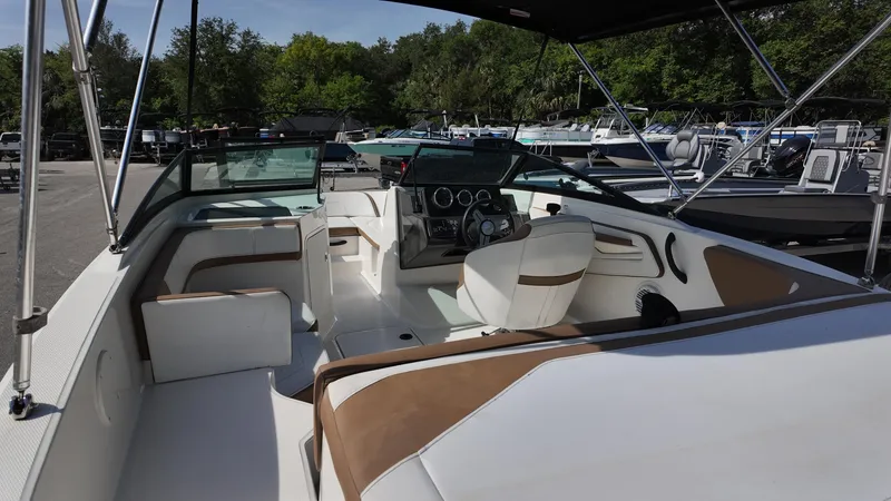 Slide: The Image of 2018 Sea Ray 190 Bow Rider interior with brown and white seating, parked outdoors. - 15