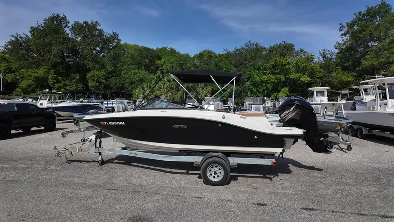 Slide: The Image of 2018 Sea Ray 190 Bow Rider boat on trailer, parked outdoors, surrounded by trees and other boats. - 21