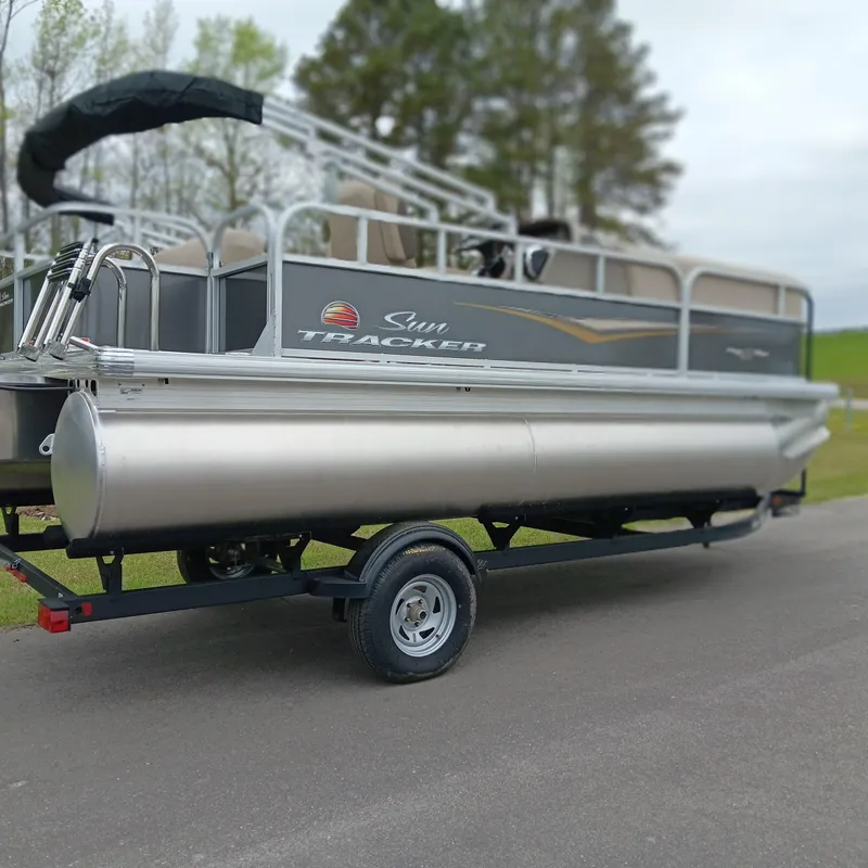 Slide: The Image of 2025 Sun Tracker Party Barge 18 DLX pontoon boat on trailer, parked outdoors. - 2