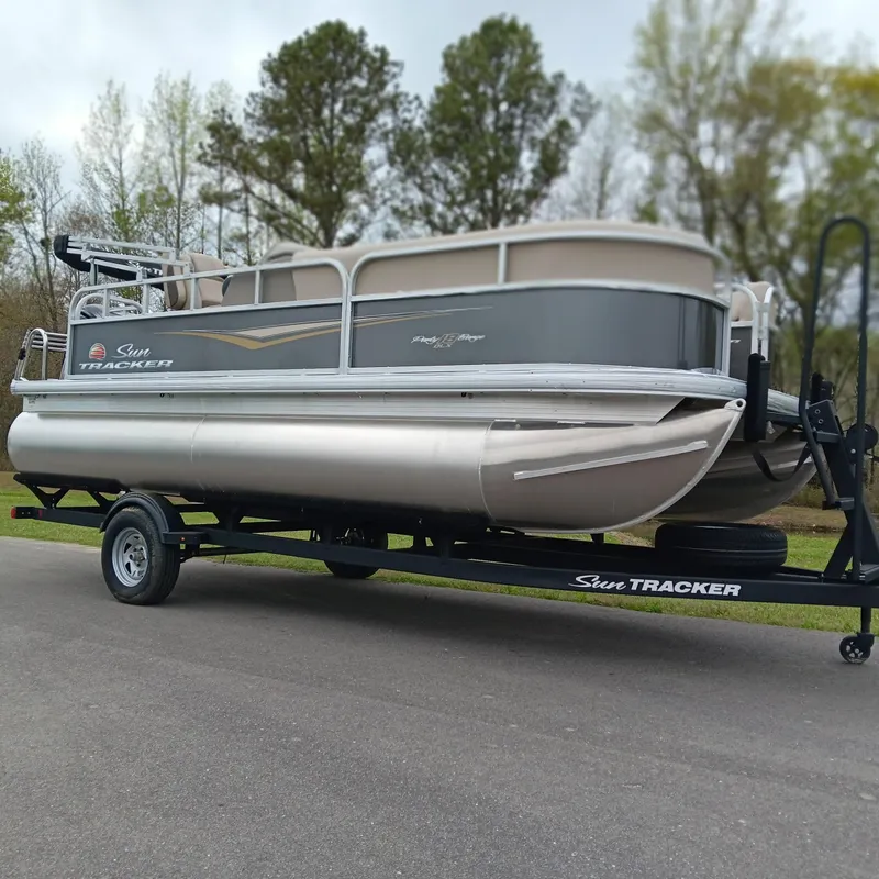 Slide: The Image of 2025 Sun Tracker Party Barge 18 DLX pontoon boat on trailer, parked outdoors. - 3
