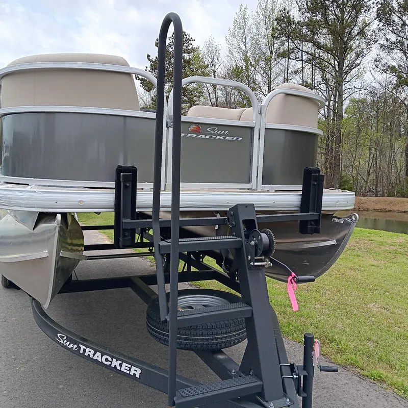 Slide: The Image of 2025 Sun Tracker Party Barge 18 DLX on trailer, parked near a wooded area. - 4