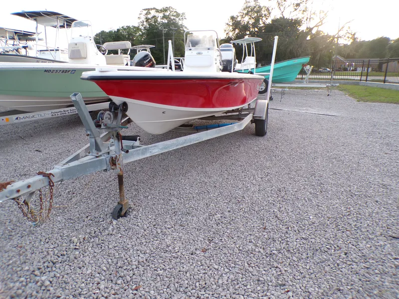 Slide: The Image of 2006 Mako 1801 Inshore boat with red hull on trailer, parked on gravel. - 2