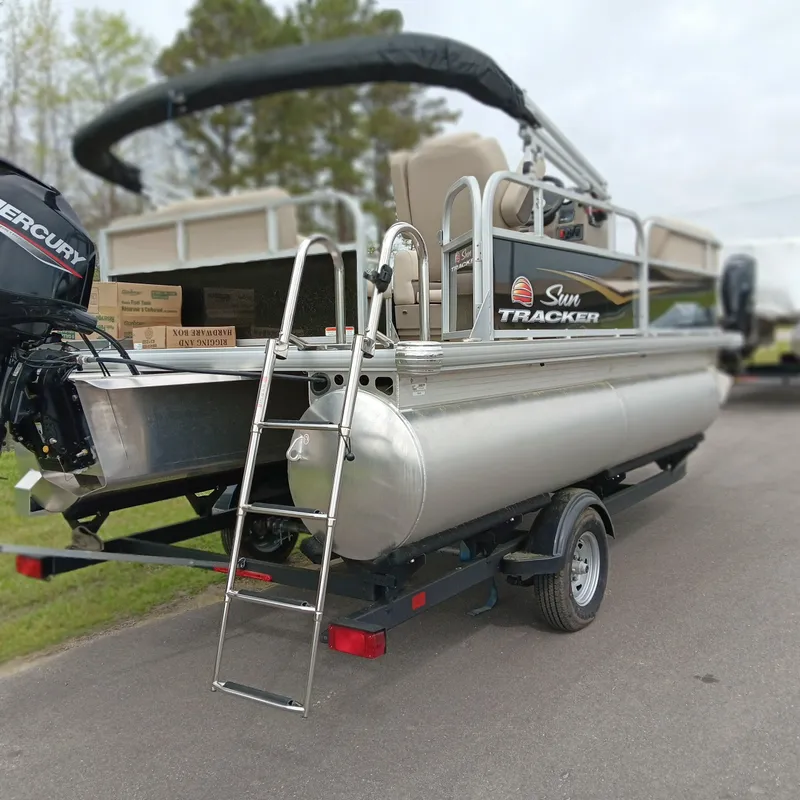 Slide: The Image of 2025 Sun Tracker Party Barge 16 DLX pontoon boat on trailer, featuring Mercury outboard motor. - 2