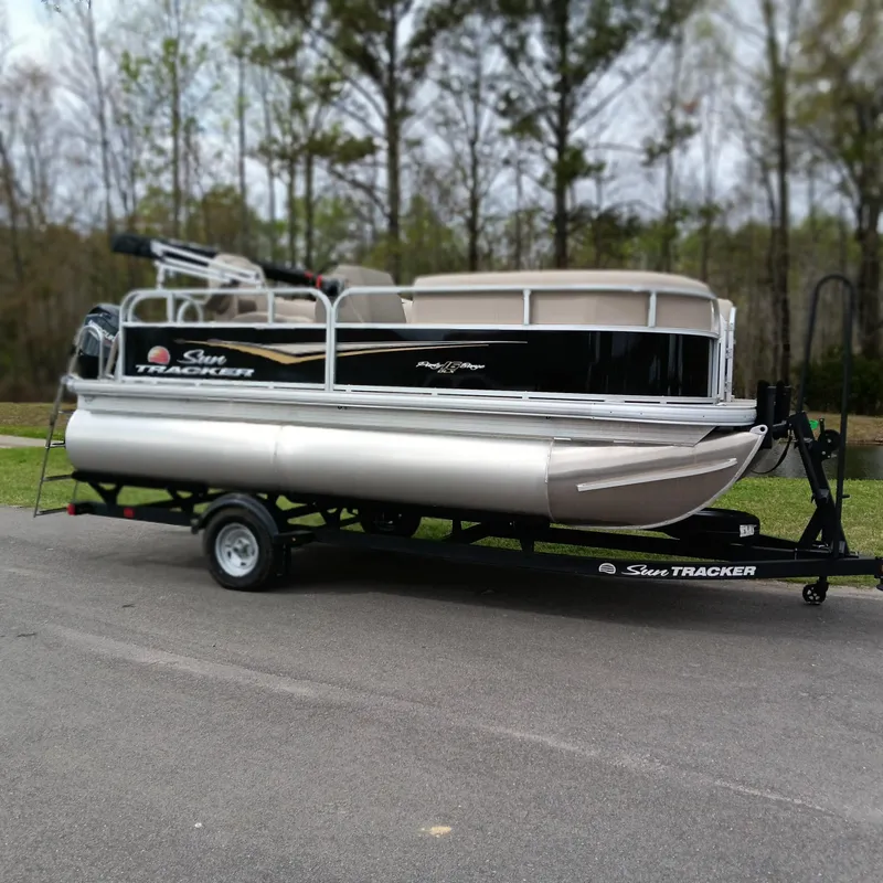 Slide: The Image of 2025 Sun Tracker Party Barge 16 DLX pontoon boat on trailer, parked outdoors. - 3