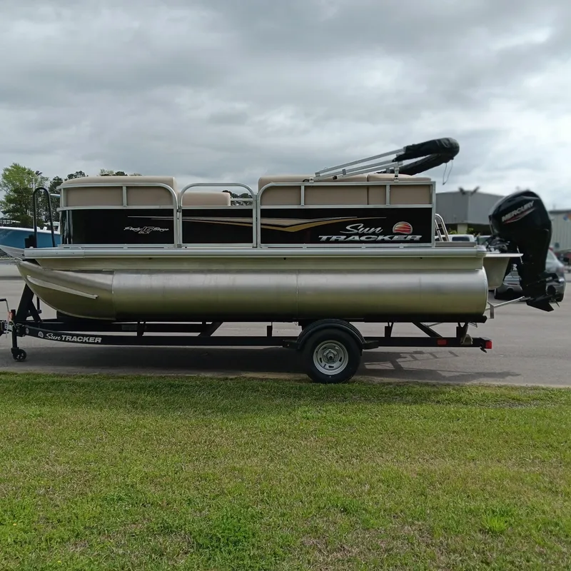 Slide: The Image of 2025 Sun Tracker Party Barge 16 DLX pontoon boat on trailer, parked outdoors. - 4