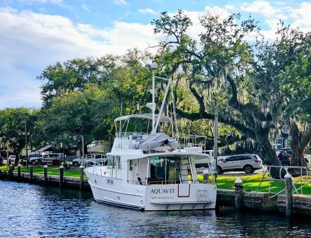 Slide: The Image of 2006 Beneteau Swift Trawler 42 docked by a scenic, tree-lined waterfront. - 2