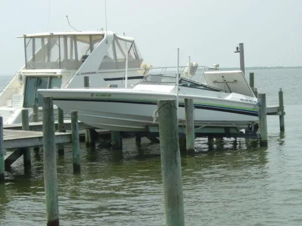 The Image of 1998 Corsa offshore flat deck boat docked beside another vessel on a calm waterway. - 0
