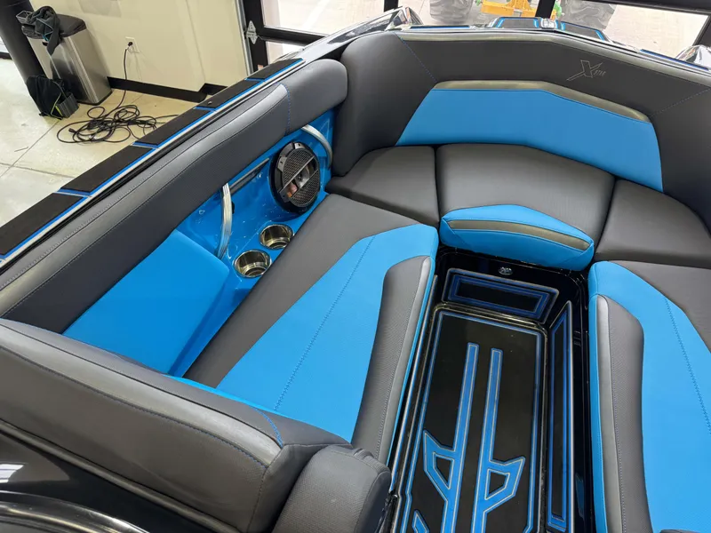 Slide: The Image of 2018 MasterCraft XStar boat interior with blue and black seating, cup holders, and speaker. - 19