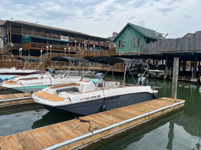 Slide: The Image of 2025 Starcraft SVX 211 OB boat docked at a marina with wooden buildings in the background. - 1